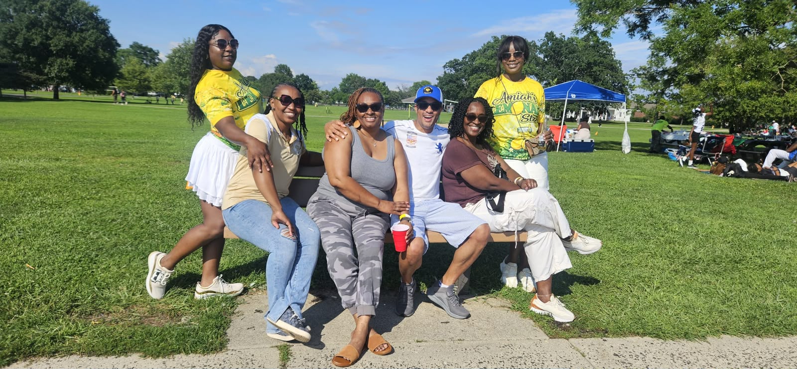 Group of friends seated on a park bench in the sunshine at the Family Fun Day picnic