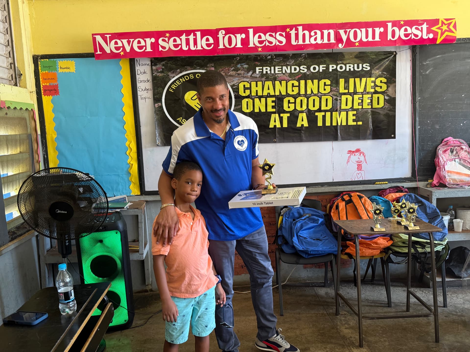 Carson Robinson, President of Friends of Porus, presenting a tablet and trophy to a student at Porus Primary School